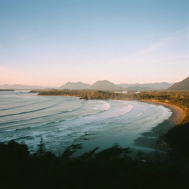 Curving bay with long lines of surf and forested headlands