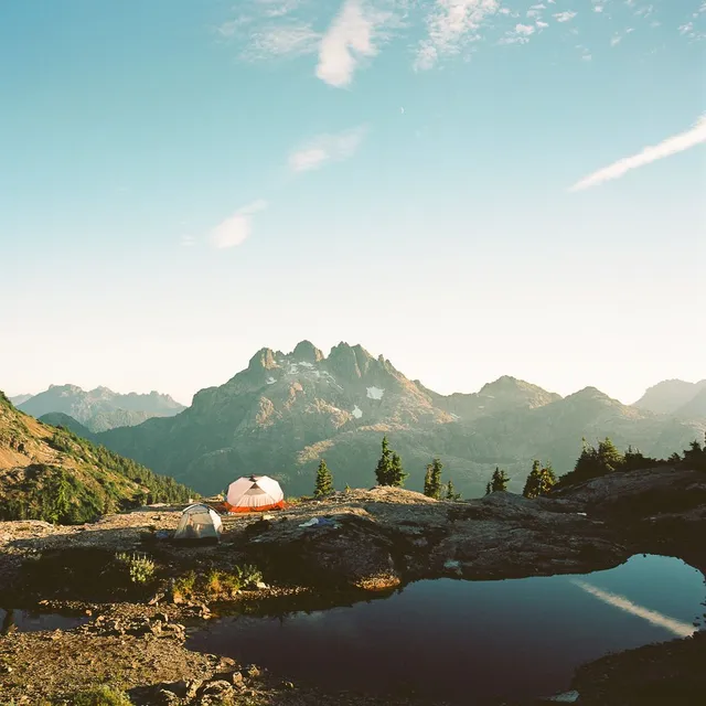 Tents on a rocky ridge beside a tarn below a jagged peak