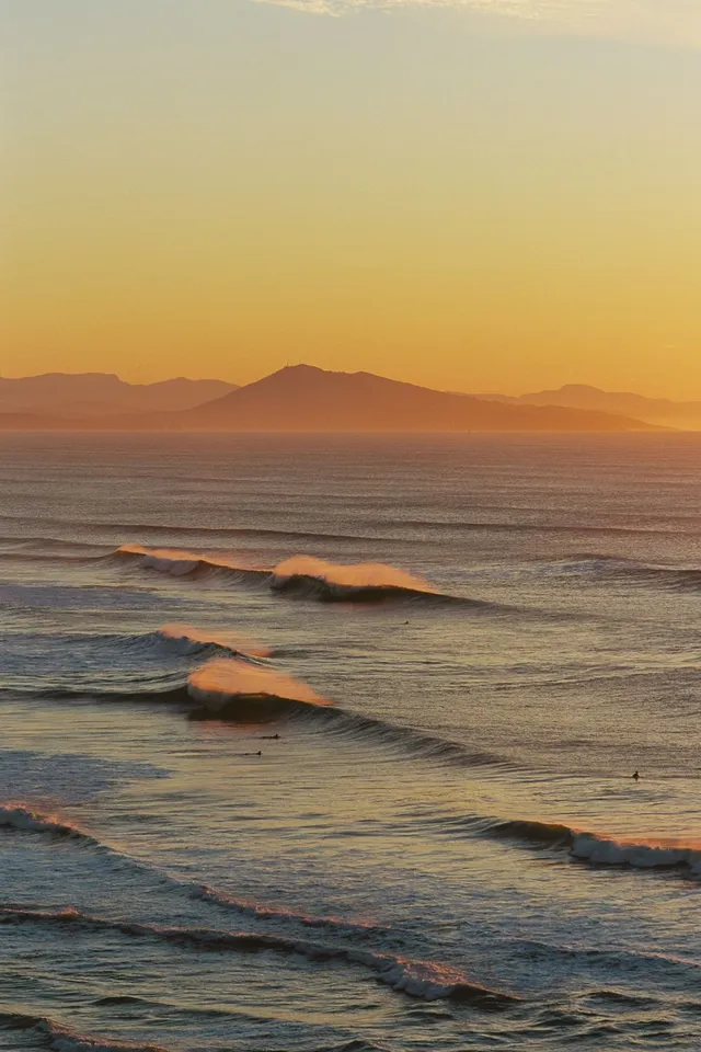 Golden evening waves rolling in below hazy mountains