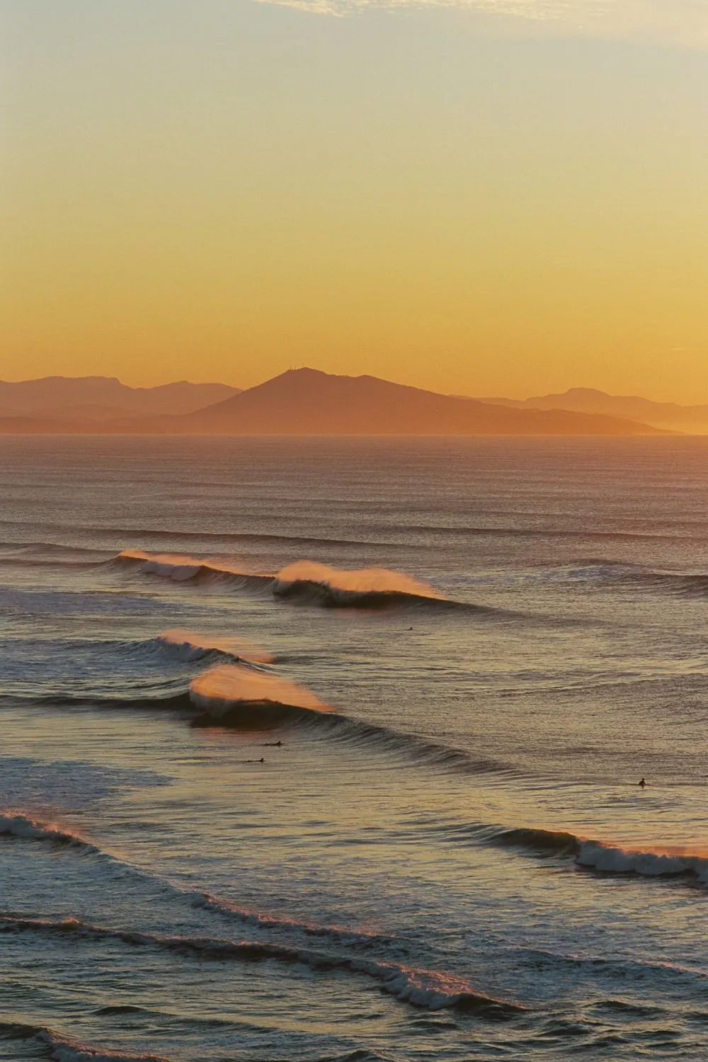 Golden evening waves rolling in below hazy mountains