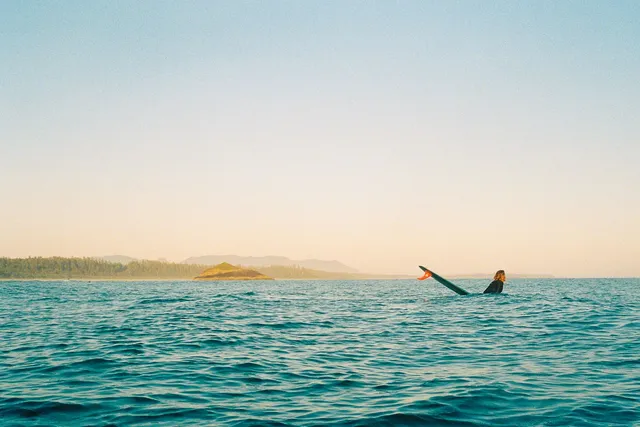 Surfer paddling on open water, coastline in the distance