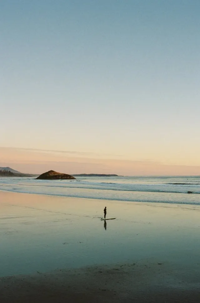 Lone surfer on a glassy beach at dusk