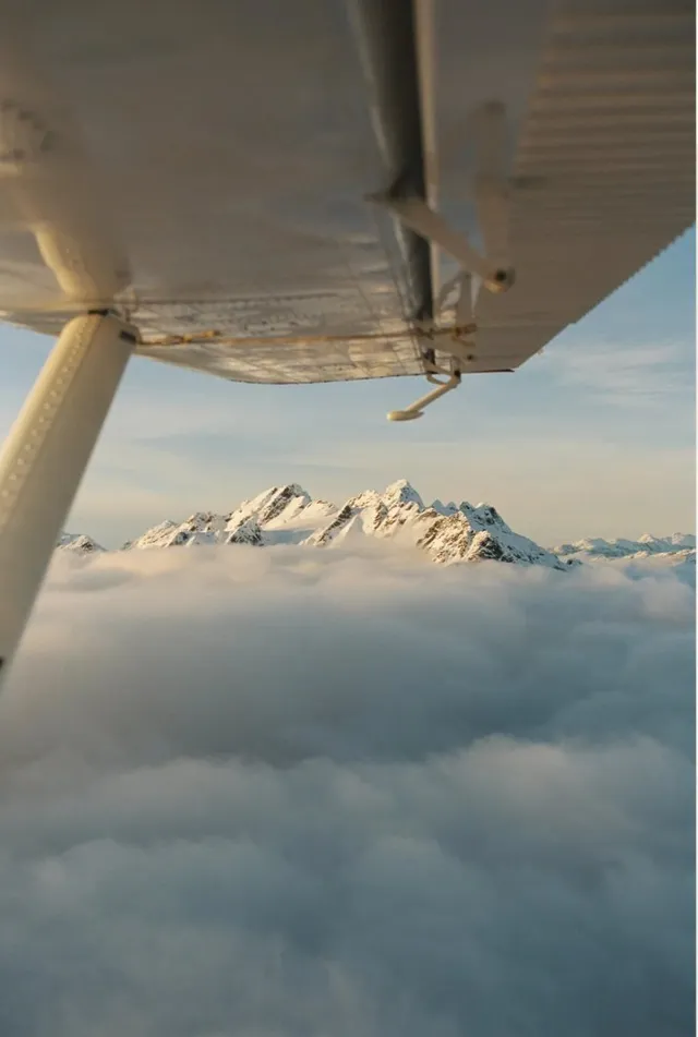Snowy peaks above clouds under a plane wing
